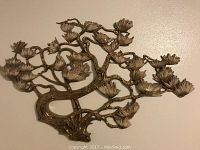 Front-facing photo of metal tree branch wall sculpture with leaves mounted on a white wall.