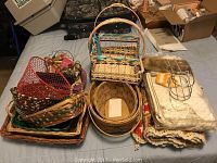 Overall view of assorted wicker baskets, folded textiles, and artificial flowers arranged on a bed.