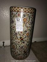 Ceramic umbrella stand showing floral vine design and wear