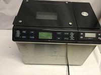 Front view of stainless steel bread maker with control buttons and glass lid.