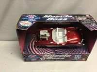 Front angled view of red metallic Muscle Boss muscle car in original box with some wear on box, visible engine detail and white interior.