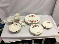 Full view of set including plates, bowls, and mugs displayed on table showing poinsettia pattern and gold edge trim.