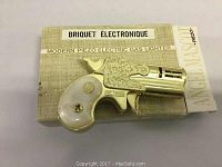 Photo of gun-shaped electric gas lighter on top of its original beige textured box labeled 'Briquet Electronique Modern Piezo Electric Gas Lighter' with brand name Angelmase.