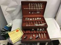 Wide view of wooden flatware box opened showing knives in upper row, forks and spoons in middle section, and serving utensils in drawer below.