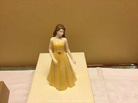 Front view of yellow dress porcelain figurine of woman representing Gemini zodiac sign.