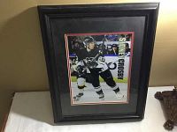 Framed picture of Sidney Crosby skating in Pittsburgh Penguins gear in black wooden frame with black and red matte borders