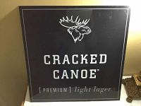 Front view of black metal Cracked Canoe beer sign with white text and moose logo.