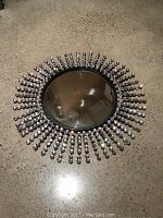 Full view of round mirror with black frame and faceted clear bead starburst embellishment.