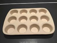 Top view of beige Pampered Chef stoneware muffin tray with 12 muffin cups showing usage marks.