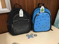 Front view of black and blue backpacks with tags and collectible charms on the front panels placed in circular holes.