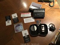 Complete No!No! hair removal system kit components arranged on a wooden surface including device, charger, comb attachments, manuals, DVD, storage case, and box.