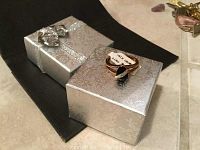 Ring resting on top of a silver patterned gift box with a bow, showing its design.