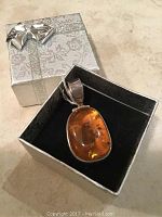 Amber stone pendant in open silver patterned gift box with bow on lid.