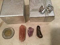 Three polished gemstone pieces displayed next to a coin and a silver gift box with bow.