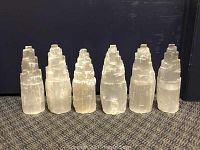 Front view of six large cut selenite crystal pieces with stepped tower-like shapes, showing slight variances in size and some surface imperfections