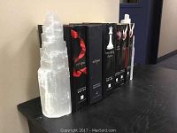 Five Stephanie Meyer hardcover books from the Twilight series and two natural salt stone bookends placed on a black shelf.