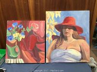 Front view of two colorful paintings on stretched canvases, one floral still life and one female portrait, displayed against a wooden background.