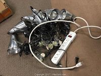 Seven silver metal clip lights with attached cords and bulbs, and a white power strip with multiple outlets and switch shown together on floor.
