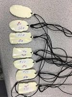 Top side view of the 7 cream-colored carved pendants laid out flat with black cords visible, showing the backside with lot numbers.
