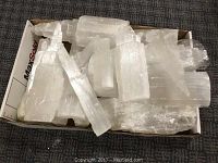Top view of a box filled with multiple white translucent selenite pieces in various forms and sizes on a textured dark surface.