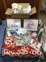 Photo of mystery box contents displayed on floral silk scarf, showing ceramic teapot, spoons, bangles, earrings, framed prints, milk glass vase, platter, and other items.