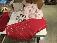 Two clear, heavy glass decanters along with red Christmas placemats and white Christmas-themed tea towels arranged on a table. Also includes a clear glass dish with a black metal stand.