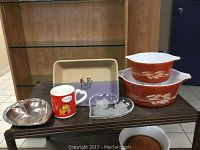Two Pyrex casserole dishes, ceramic rooster tray, Garfield mug, glass and silver heart dishes on a table.