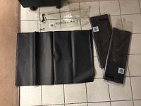 Three packages of black tissue paper sheets on tiled floor. Two packages intact and sealed, one package opened with tissue paper sheets unfolded for display.