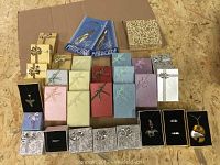 Assortment of 28 velvet-lined jewelry boxes in various colors and sizes along with necklaces, rings, brooches displayed on black velvet cushions inside some boxes, and two unopened gold beauty tweezers in original packaging.