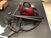 Red Shark Professional Hand Surface Steam Cleaner main unit with attached black hose and multiple black nozzle attachments, lying on a table.