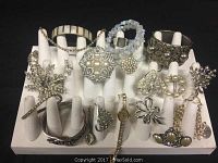 Display of over 22 vintage jewelry pieces on a white ring display board, showing brooches, bracelets, earrings, a watch, and rings, all in silver or pearl tones with rhinestone highlights. Jewelry appears complete with no missing rhinestones.
