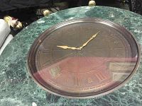 Top view showing central metal clock with Roman numerals and brass hands set into green marble surface