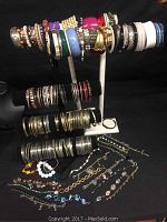 Bracelets and bangles displayed on black and white bracelet display stands and laid out on flat black surface including various styles and materials.