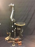 Full view of all lot items including giraffe, elephants, side table with human figure base, brass pelican, and smaller human figure