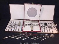 Three open boxes containing vintage cutlery sets including forks, pie servers, and spoons, laid out on a black surface.