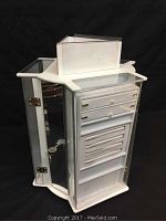 Front angle showing the white revolving 3-sided display case with clear, lockable doors, internal organizers and keys in lock