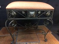 Side angle of modern cast iron ottoman showing coral fabric top and detailed leaf motif metal work on sides and legs.