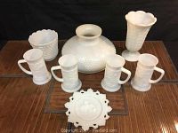 Eight pieces of vintage milk glass including a lampshade, mugs, two vases, and decorative plate.
