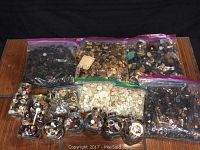 View showing a collection of assorted buttons contained in multiple large zip-lock bags and several clear jars, placed on a wooden surface with a black background.