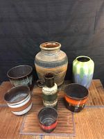 Seven ceramic pottery pieces in various shapes and colorful glazes arranged on a wooden surface.