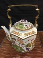 Side view of the porcelain tea pot showing detailed floral and bird design with heavy brass handle