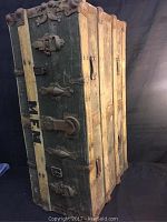 Antique wooden chest standing upright, showing metal hinges and latches, marked with letters 'M.F.M.'