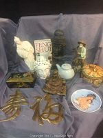 Photo showing all items arranged on cloth, including statues, brass characters, Buddha heads, teapot, figurine, decorative plate, and Feng Shui book.