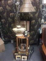 Wide view showing wooden giraffe-pattern table, tall giraffe figurine, lamp with bamboo style base, chef figurine, and picture frames.