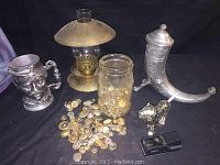 Full view of jar of assorted antique buttons, pewter mug with detailed face, brass candle lamp, metal horn with lid, mother of pearl lion figurine, and a black stapler.
