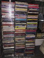 Six stacks of music CDs showing a wide variety of titles and artists, general overview of the entire lot.