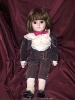 Full view of the entire doll showing clothing and posture against a red cloth background.