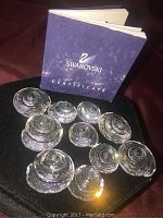 Set of 10 clear Swarovski crystal shells displayed on a black surface with a Swarovski certificate booklet in background, showing clarity and spiral design of shells.