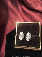Pair of tear drop-shaped Swarovski crystal earrings displayed on a brown velvet cushion inside a gold-trimmed box.