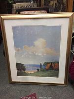 Full view of the framed print showing the coastal landscape scene under glass in a gold-toned frame.